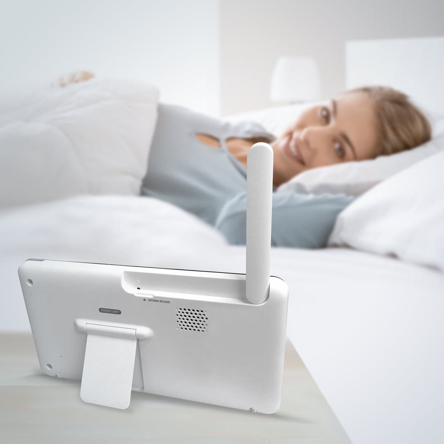 A person in bed looks at a white electronic device, a baby monitor parent unit, on a nightstand