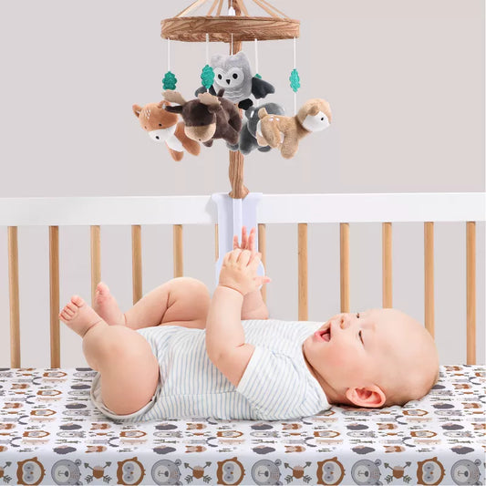 Baby in a crib looking at a hanging crib mobile with woodland-themed animal toys