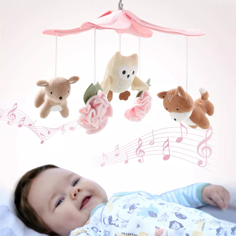 A baby lies beneath a pink floral baby mobile with plush deer, owl, and fox toys