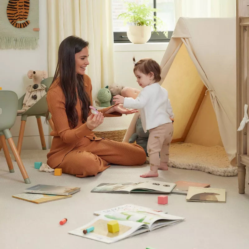 A woman and a child are playing on the floor near a play tent and open books