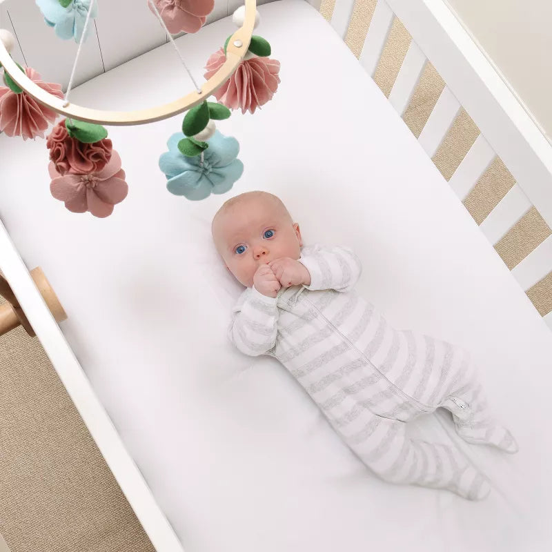 Baby in a crib looking up at a floral mobile with pink and blue flowers hanging above
