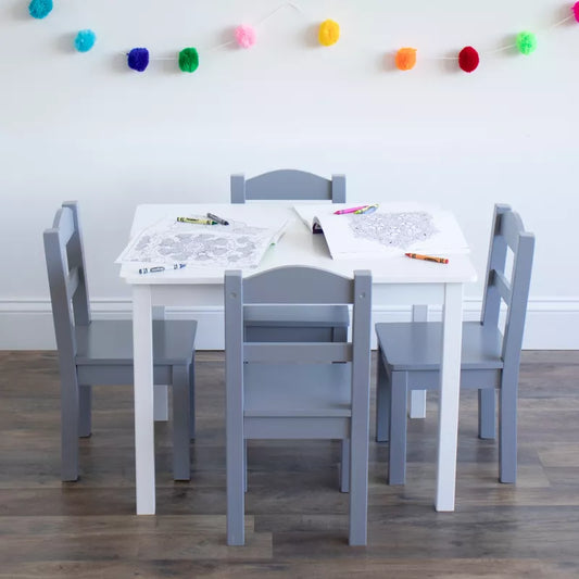 A white kids' table with four grey chairs, coloring pages, and crayons, adorned with pom-pom garland
