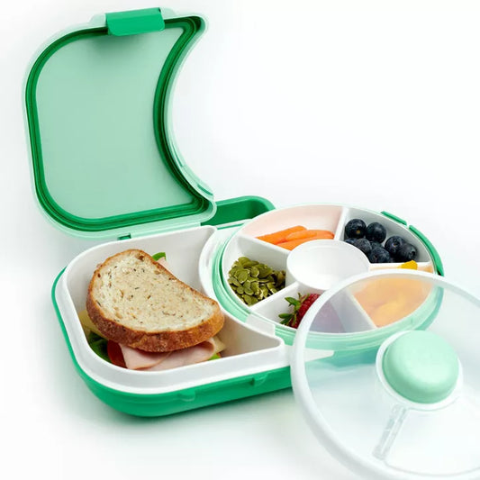 Green and white bento lunch box with compartments containing a sandwich and various snacks on a white background