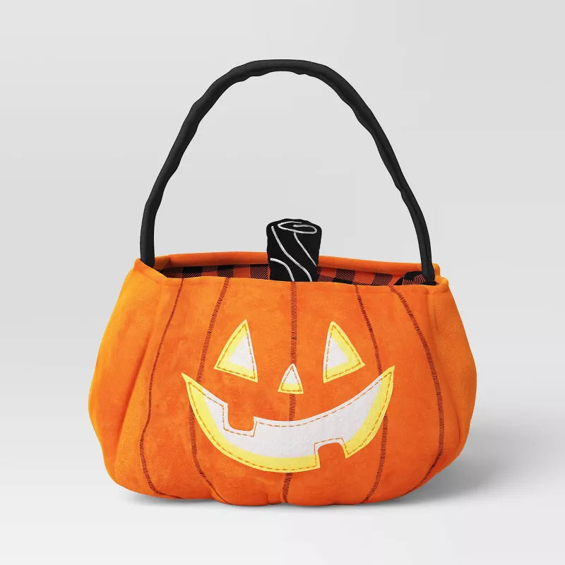 Orange pumpkin-shaped Halloween candy basket with a black handle on a light gray background