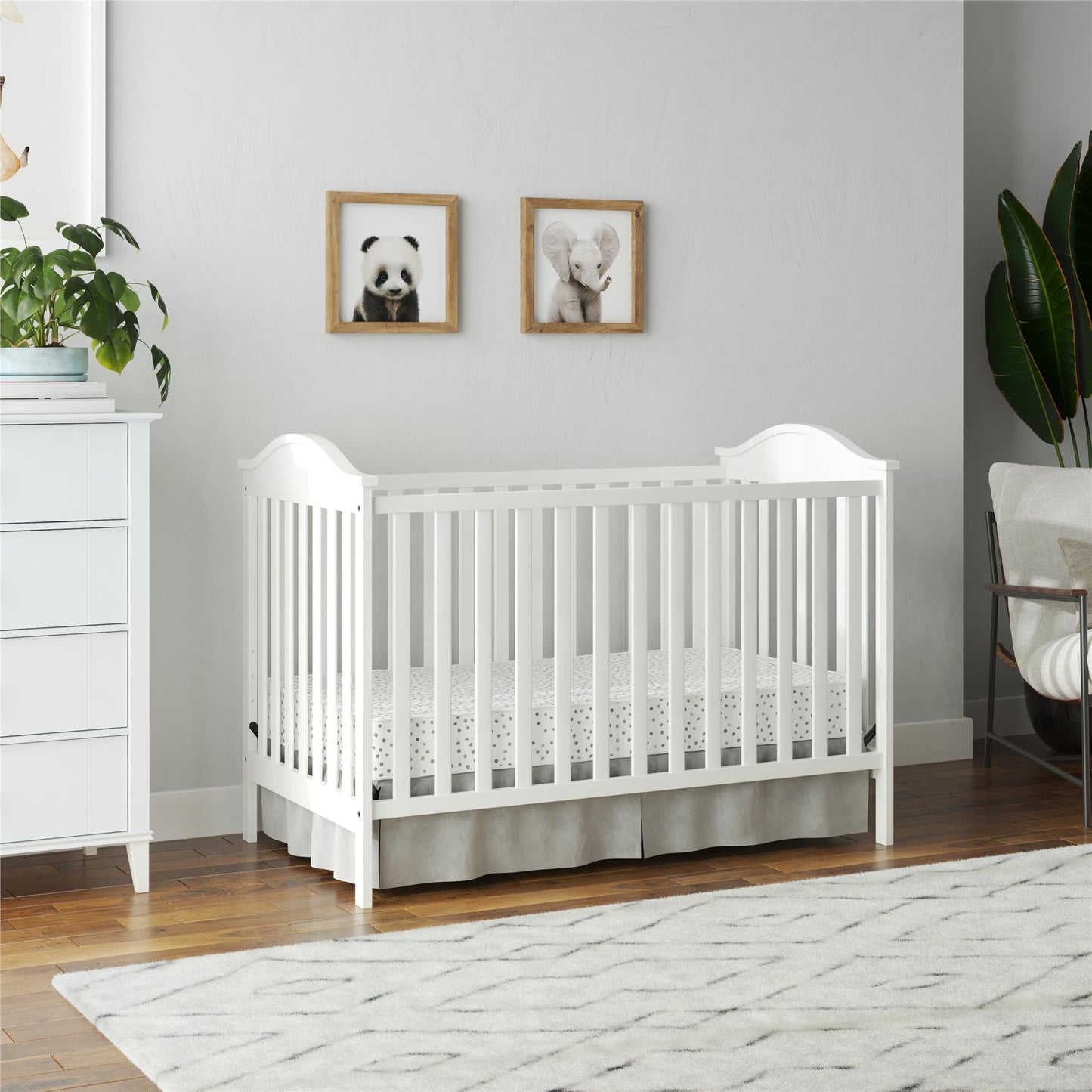 A white baby crib with a patterned mattress and skirt, situated in a nursery