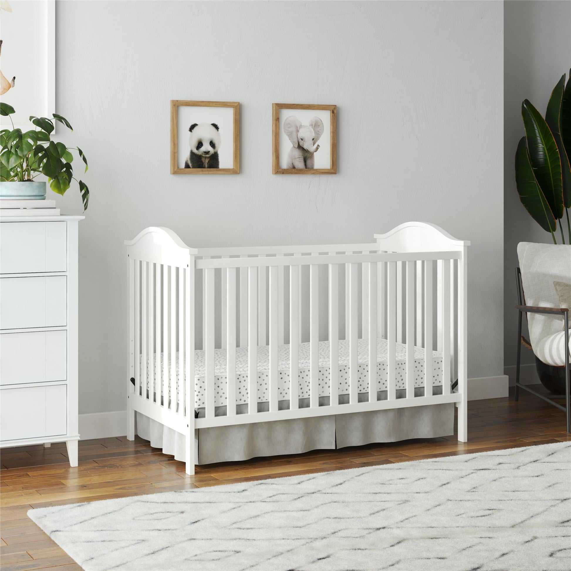 A white baby crib with a patterned mattress and skirt, situated in a nursery
