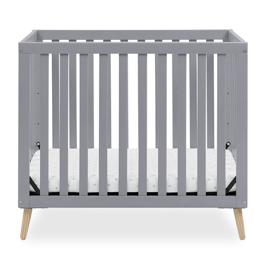 A grey baby crib with a white mattress, featuring natural wood splayed legs