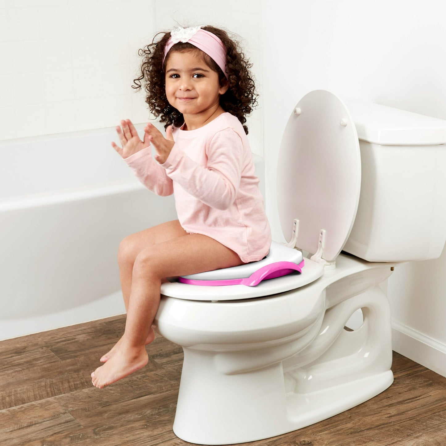 A young child sits on a toilet with a pink potty seat in a bathroom