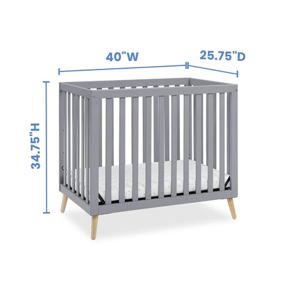 A gray baby crib with natural wood legs and mattress, displaying height, width, and depth dimensions