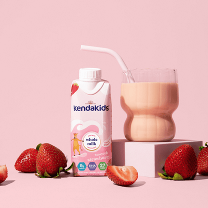 A carton and glass of strawberry flavoured nutritional drink for kids with fresh strawberries on a pink background