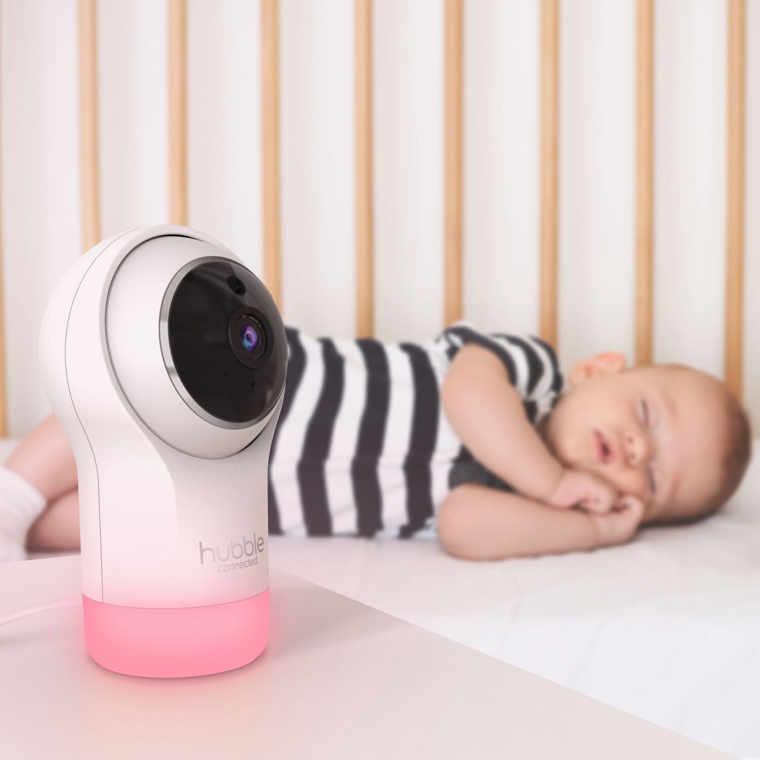 A baby sleeps in a crib while a baby monitor sits nearby