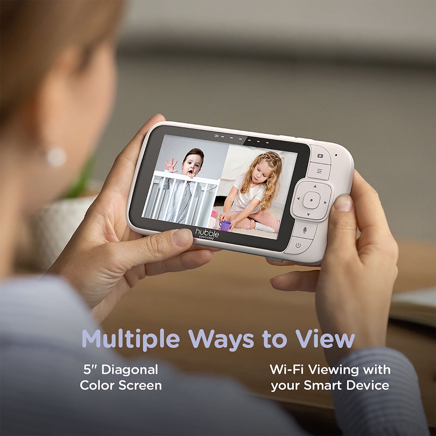 Person holding a baby monitor displaying two children on its screen, connected to smart devices