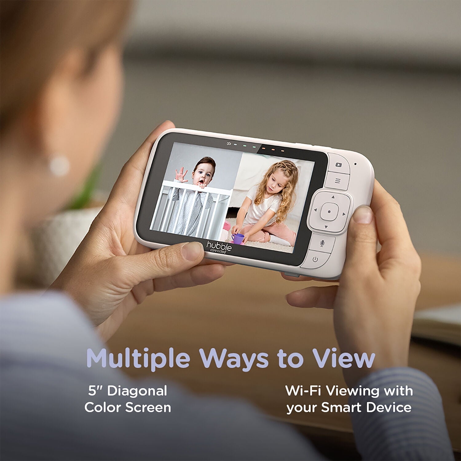 Person holding a baby monitor displaying two children on its screen, connected to smart devices