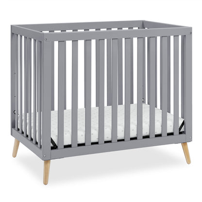 A grey baby crib with a mattress, featuring wooden legs and slatted sides