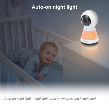 A baby in a crib next to a baby monitor with an auto-on night light feature