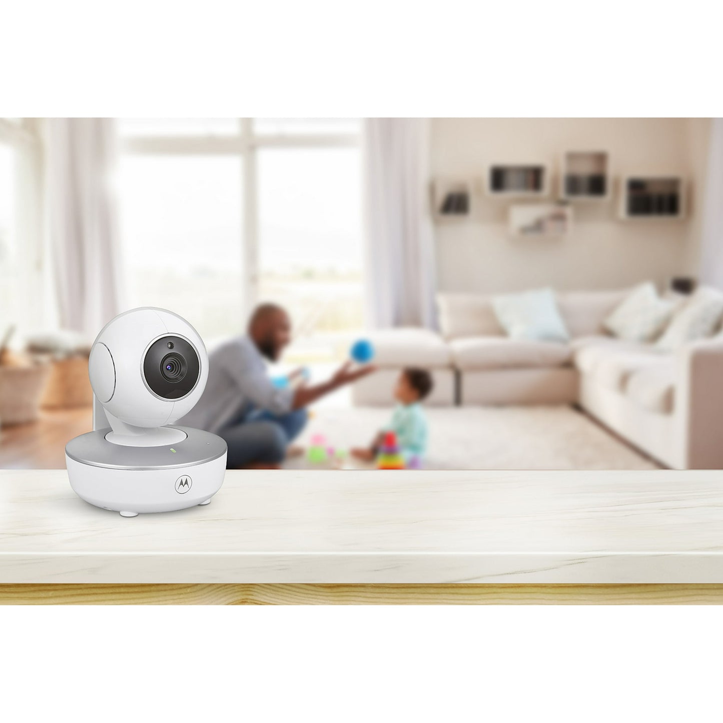 A baby monitor camera on a table with a blurred background of an adult and child playing