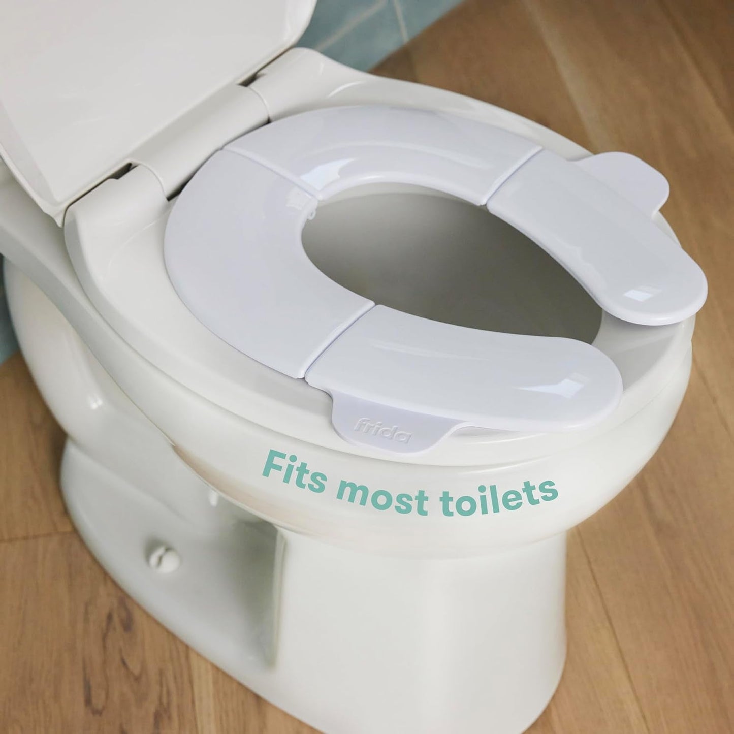 A white, foldable potty seat is placed on a white toilet, on a wooden floor