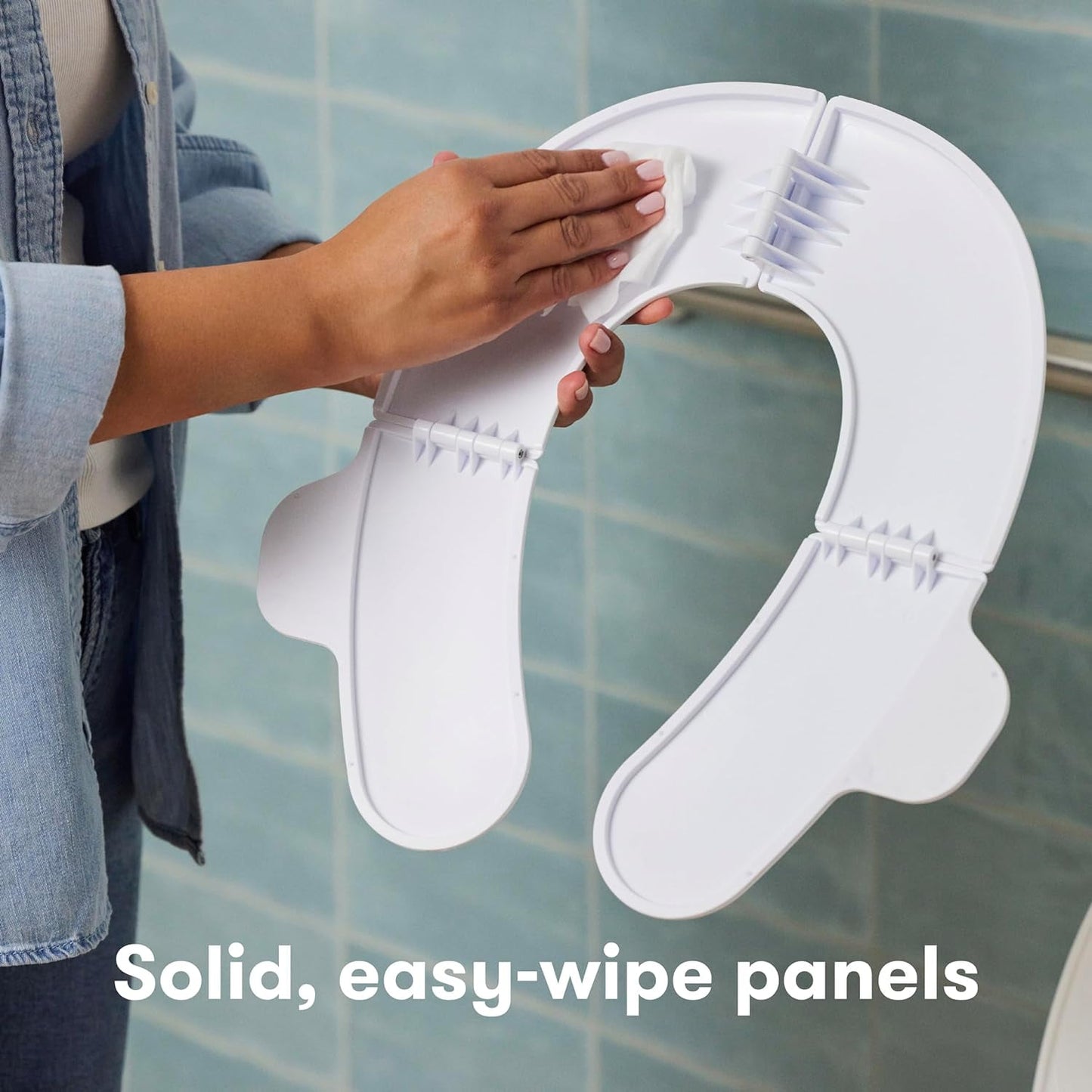 Hands clean a white, foldable potty seat, featuring solid, easy-wipe panels