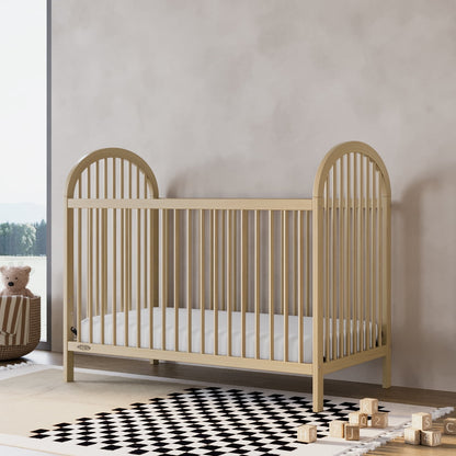 A light-colored wooden baby crib with a mattress in a nursery room setting