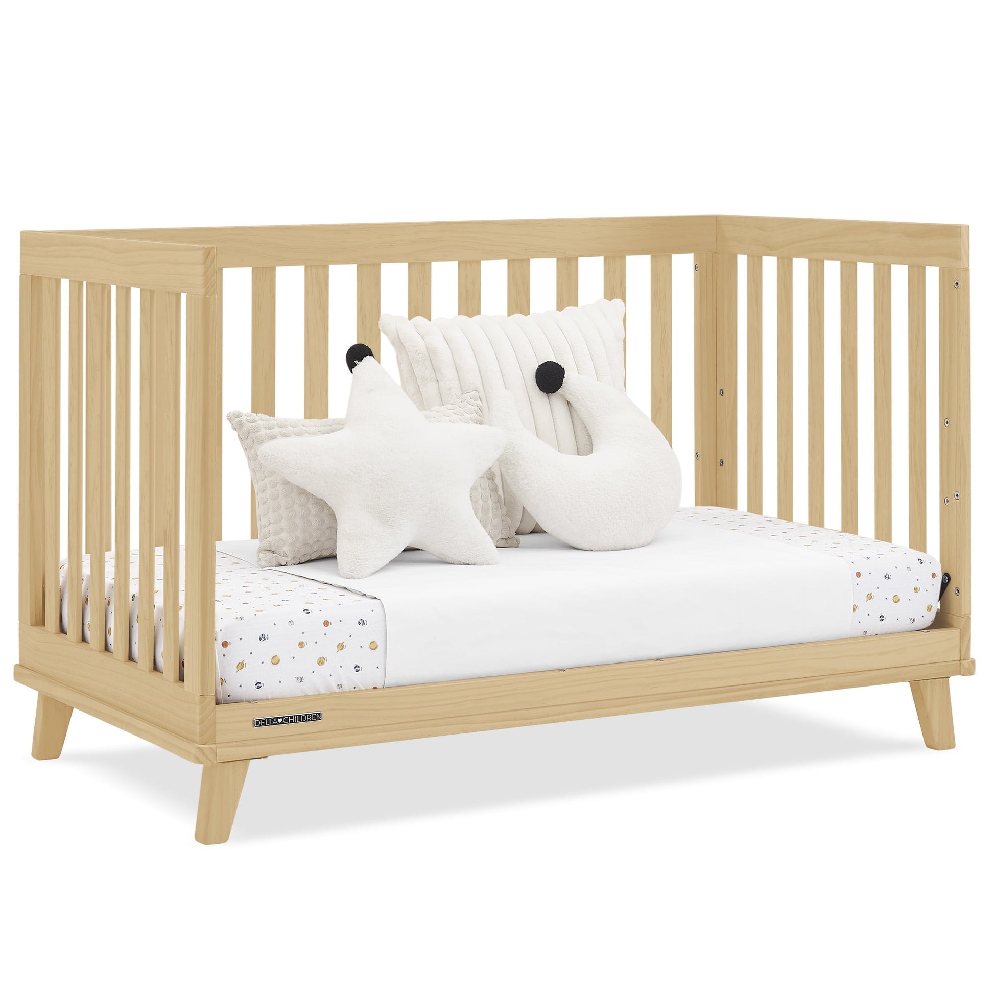 A light wood baby crib with a white mattress, patterned sheet, and decorative pillows