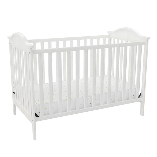A white wooden baby crib with a patterned mattress in a brightly lit setting