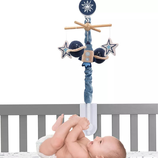A baby laying in a crib and a baby musical crib mobile featuring a rocket, planets, and stars hanging above