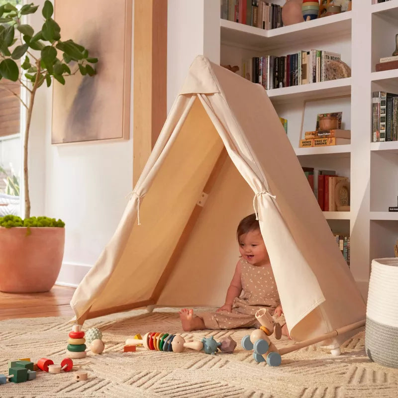 A baby sits inside a play tent on a rug, surrounded by various toys