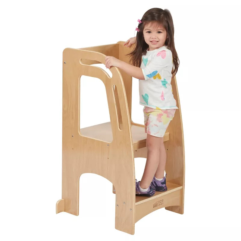 A young girl stands on a wooden children's kitchen helper tower