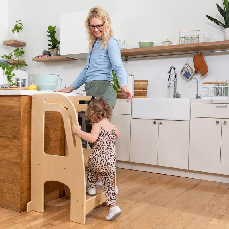 A woman and a child in a kitchen, with the child using a wooden learning tower