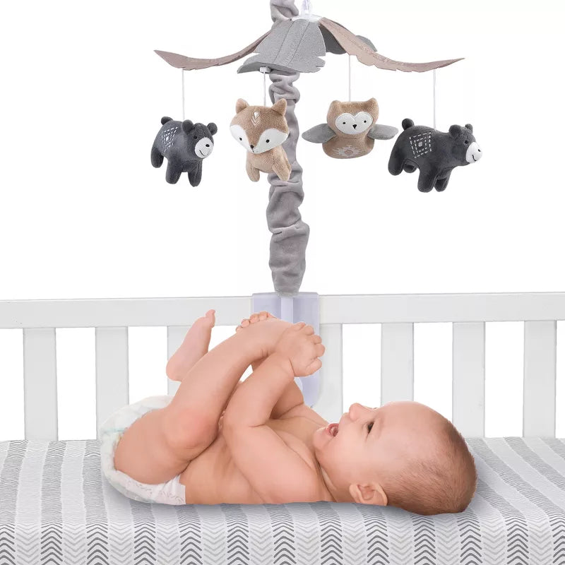 A baby lies in a crib with a musical mobile featuring woodland animals overhead