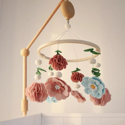 A wooden baby crib mobile hangs with felt flowers and leaves in pastel colors