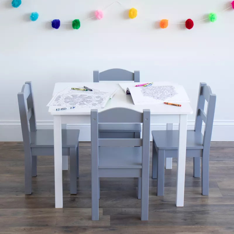 A white kids' table with four grey chairs, coloring pages, and crayons, adorned with pom-pom garland