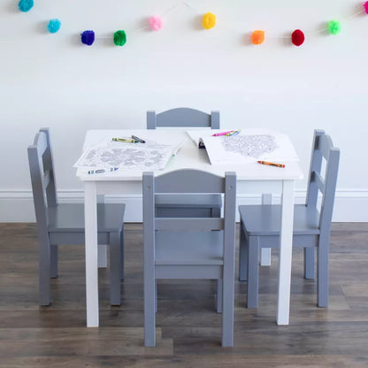 A white kids' table with four grey chairs, coloring pages, and crayons, adorned with pom-pom garland