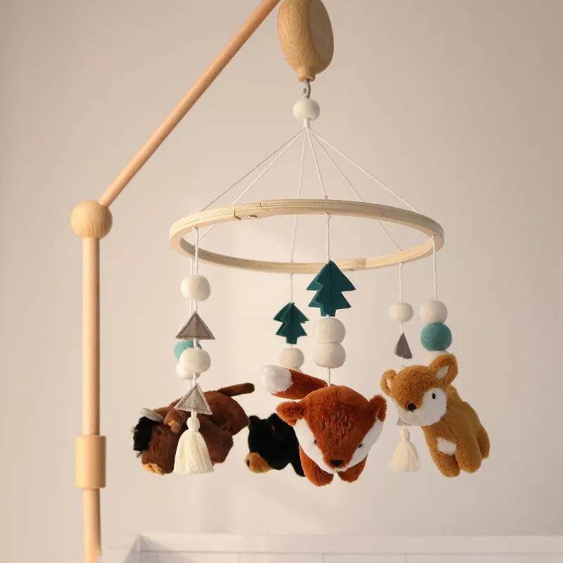 A wooden baby crib mobile hangs, featuring plush woodland animals, felt trees, and decorative balls