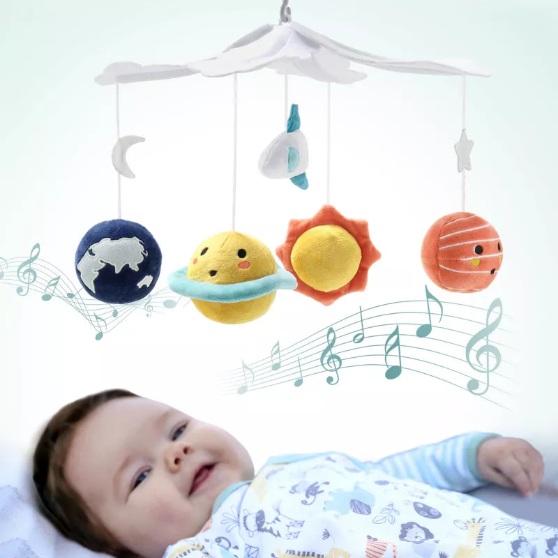 A baby lies beneath a musical crib mobile featuring planets, a sun, moon, star, and rocket