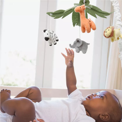 Baby in a crib reaching towards a mobile with hanging safari animal toys and green leaves