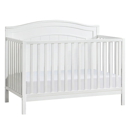 A white wooden baby crib with slatted sides and a curved headboard, containing a white mattress