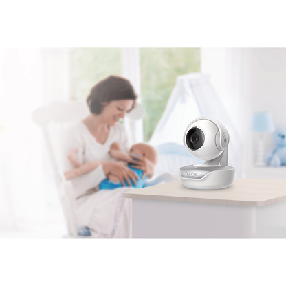 A baby monitor camera on a table with a blurred background of a parent holding a baby