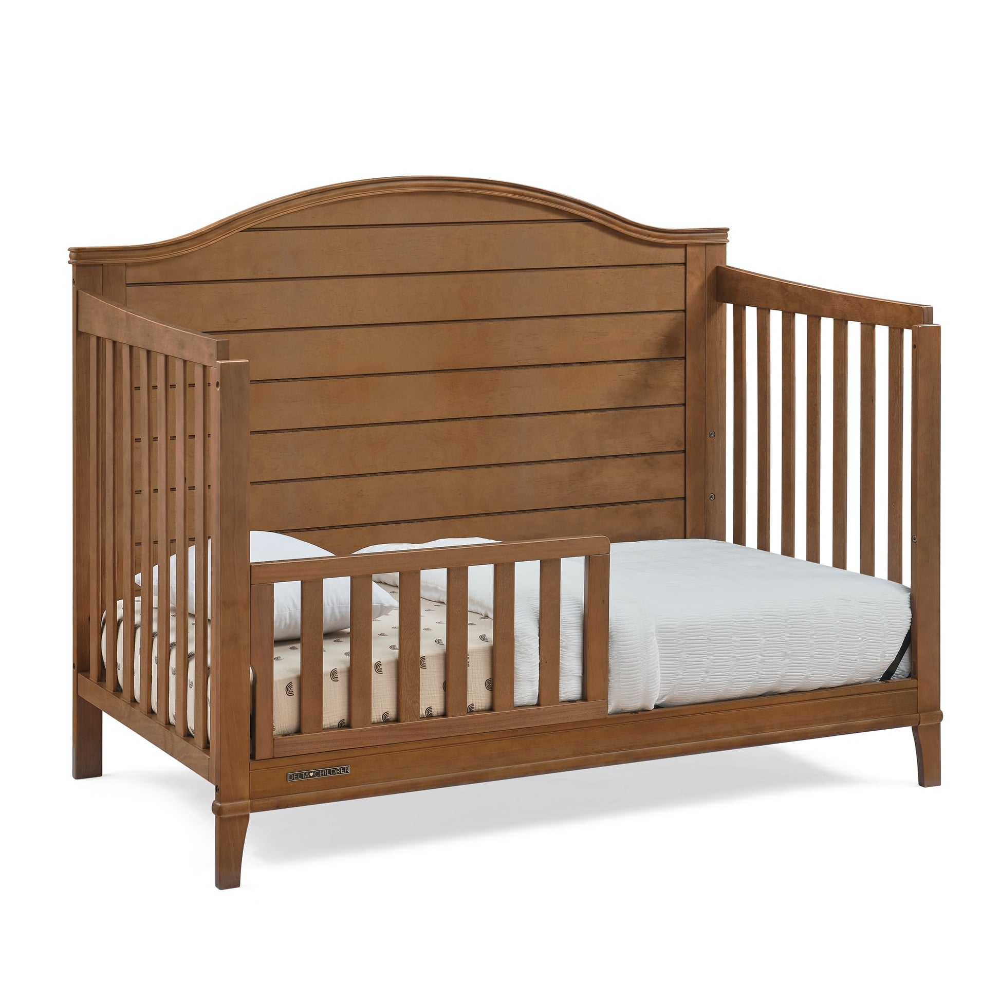 A wooden convertible crib set up as a toddler bed with a mattress and bedding