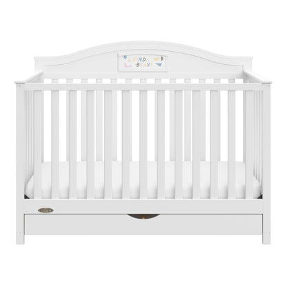 A white baby crib with vertical slats, a curved headboard, and a storage drawer underneath