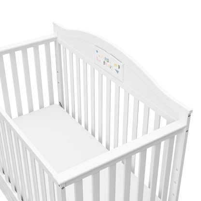 A white wooden baby crib with a decorative headboard panel