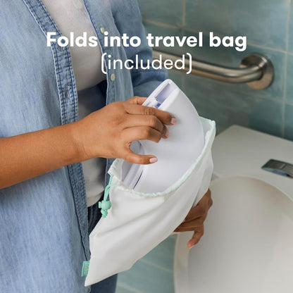 A person places a white foldable potty seat into a light-colored travel bag