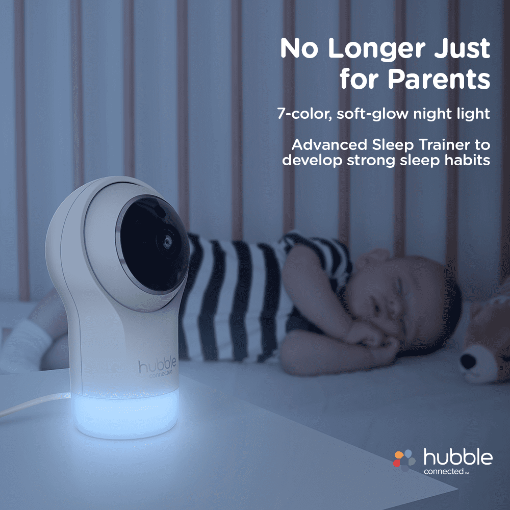 A baby monitor with a glowing base stands beside a sleeping infant in a crib