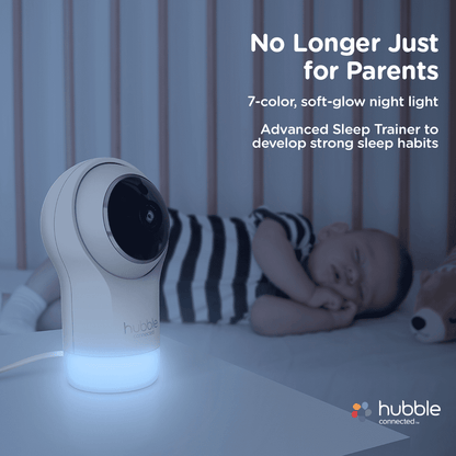 A baby monitor with a glowing base stands beside a sleeping infant in a crib